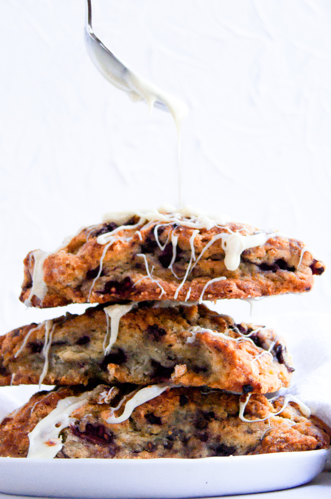 Three scones stacked on a plate with a silver spoon drizzling white chocolate on them