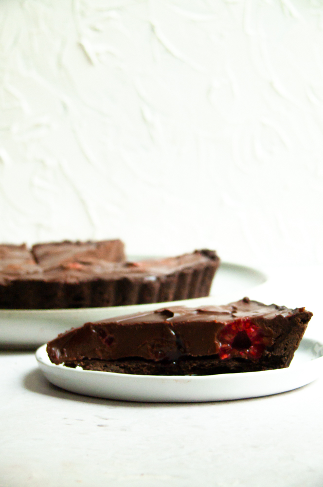 One slice of chocolate tart with berry in the middle showcased with the rest of tart behind it