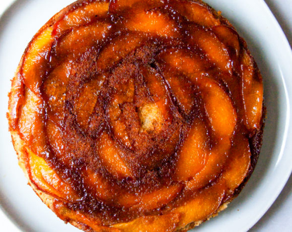 The whole peach cake on a white plate and strong lighting.