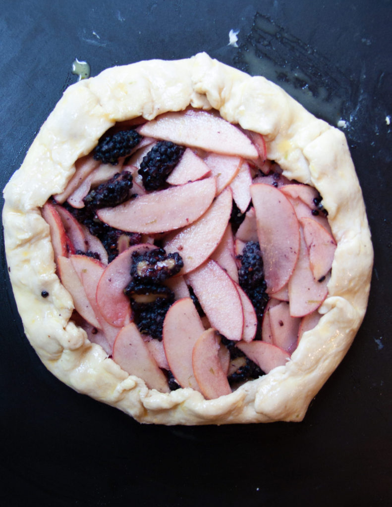 Unbaked and assembled apple galette on a black baking sheet