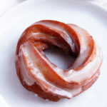 A singular crullers on a white plate with maple glaze drizzling down it
