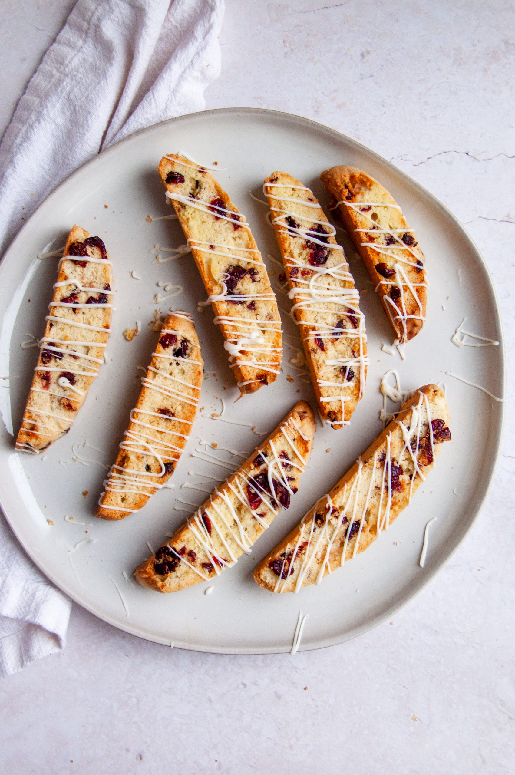 All the biscotti laid out on a white plate drizzled with white chocolate